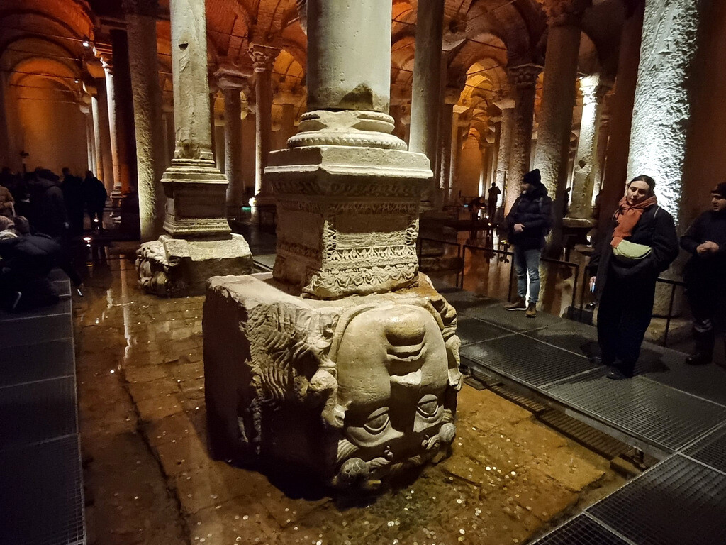 Foreign tourists admiring the Medusa Heads inside the Basilica Cistern while ancient columns and red lighting reflect across the vaulted ceiling in the background. photo by Serhat Engul
