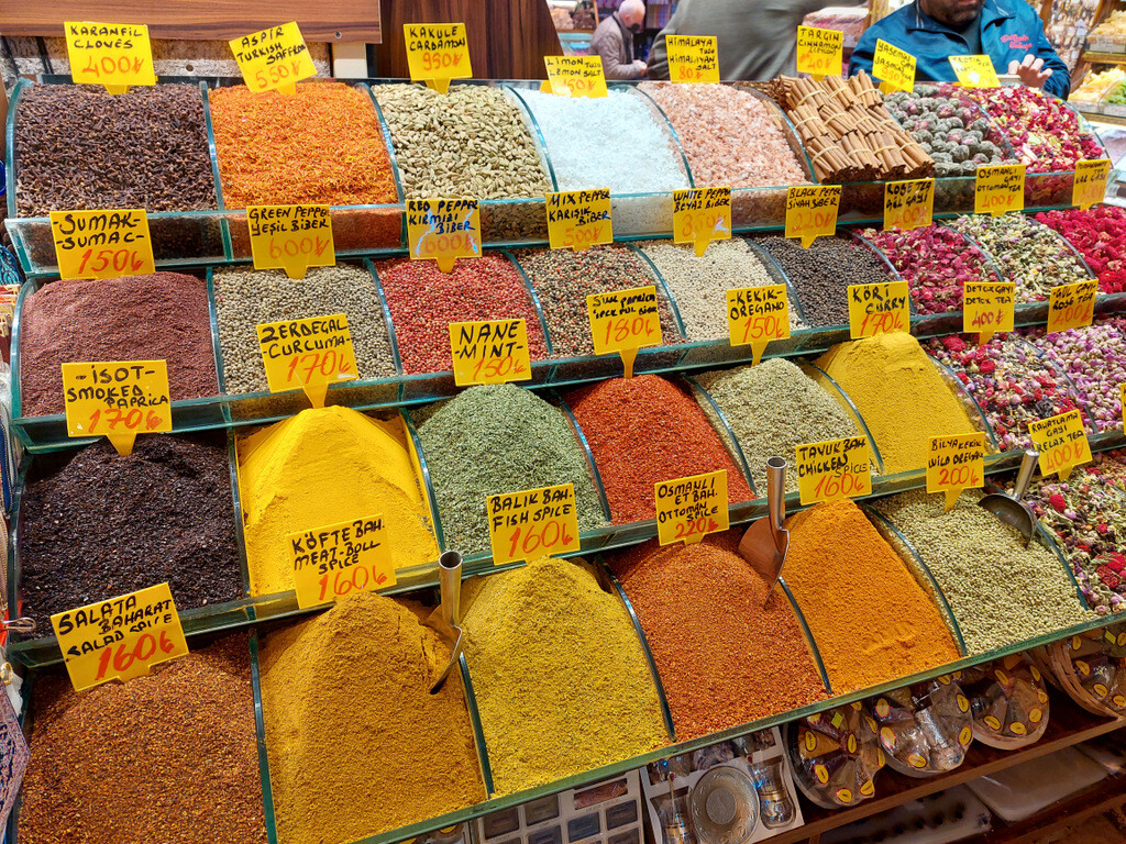 Colorful spices and tea leaves displayed in small containers outside a shop in the Spice Bazaar, with handwritten signs showing their names and prices. photo by Serhat Engul