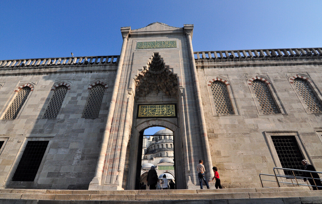 Blue Mosque monumental gate with elegant muqarnas decoration, framing the mosque’s cascading full, half, and quarter domes like a curtain. photo by Serhat Engul